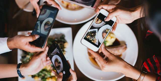 Ein Foto von mehreren Händen die ein Handy halten und Fotos von ihrem Essen machen