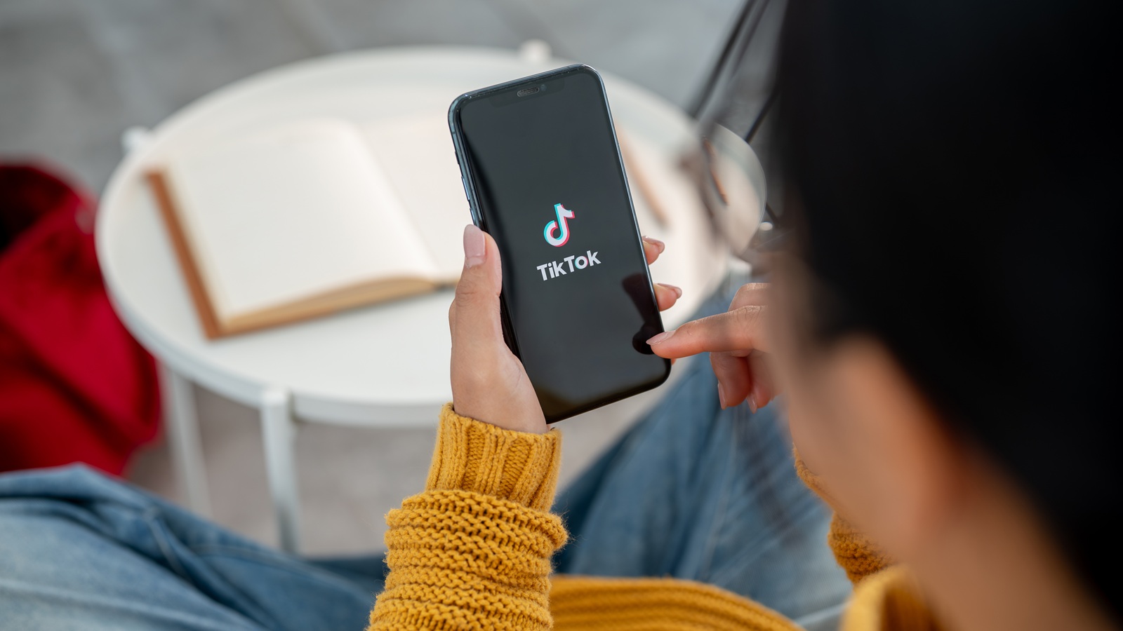 Eine Frau hält ein Smartphone in der Hand, auf dem sich gerade die TikTok App öffnet.