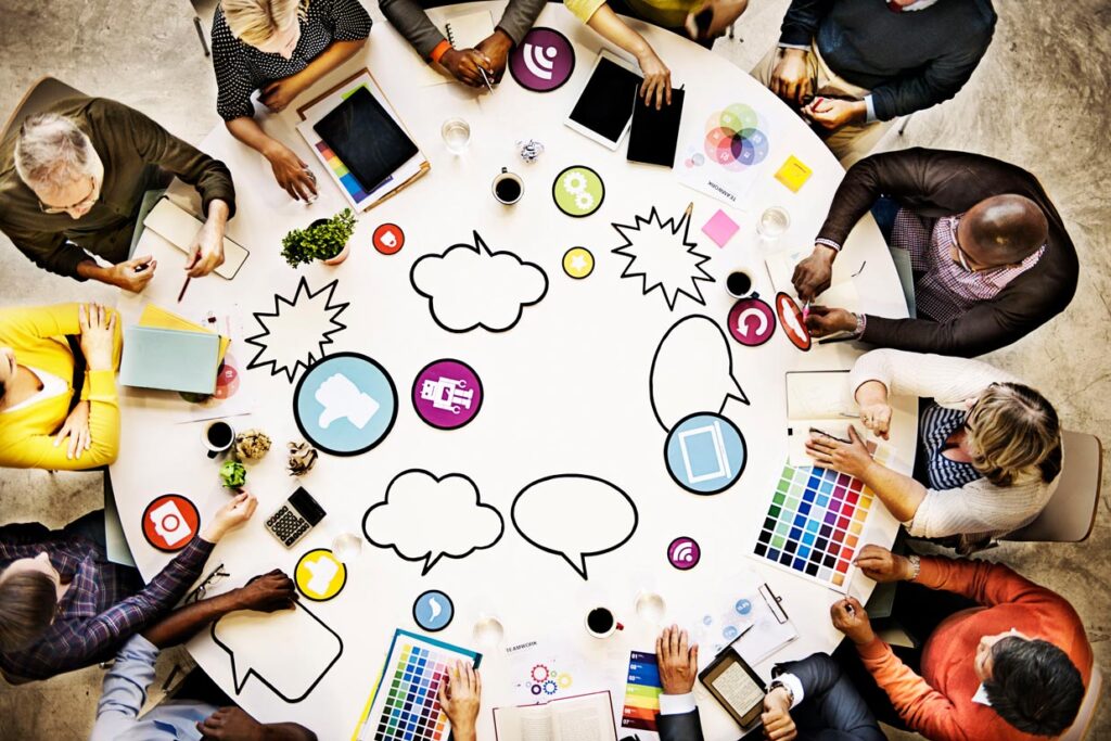 Ein großer kreisrunder Meetingtisch mit Leuten, die sich über Content briefen.