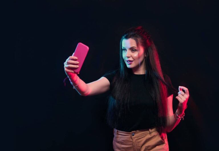 TikTok Format - Junge Frau posiert mit Smartphone in den Händen, machen Selfie auf schwarzem Hintergrund