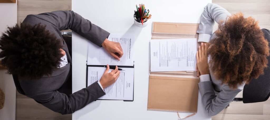 Weiterbildungen im Lebenslauf Recruiter und Bewerberin führen ein Vorstellungsgespräch, die Bewerbungsunterlagen haben sie vor sich auf dem Tisch ausgebreitet