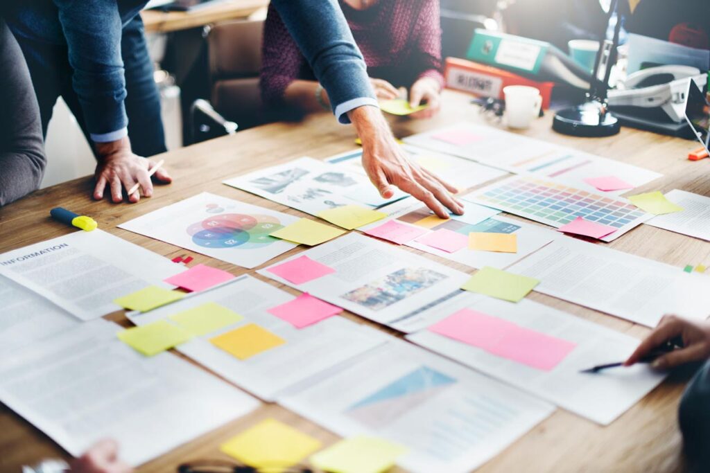 Ein großer Tisch auf dem verschieden Dokumente für ein Briefing verteilt sind an dem Leute sitzen. Artikelbild Instagram Strategie