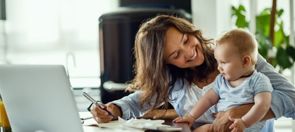 Wiedereinstieg Elternzeit Glückliche Mutter spricht mit ihrem Baby während der Arbeit zu Hause