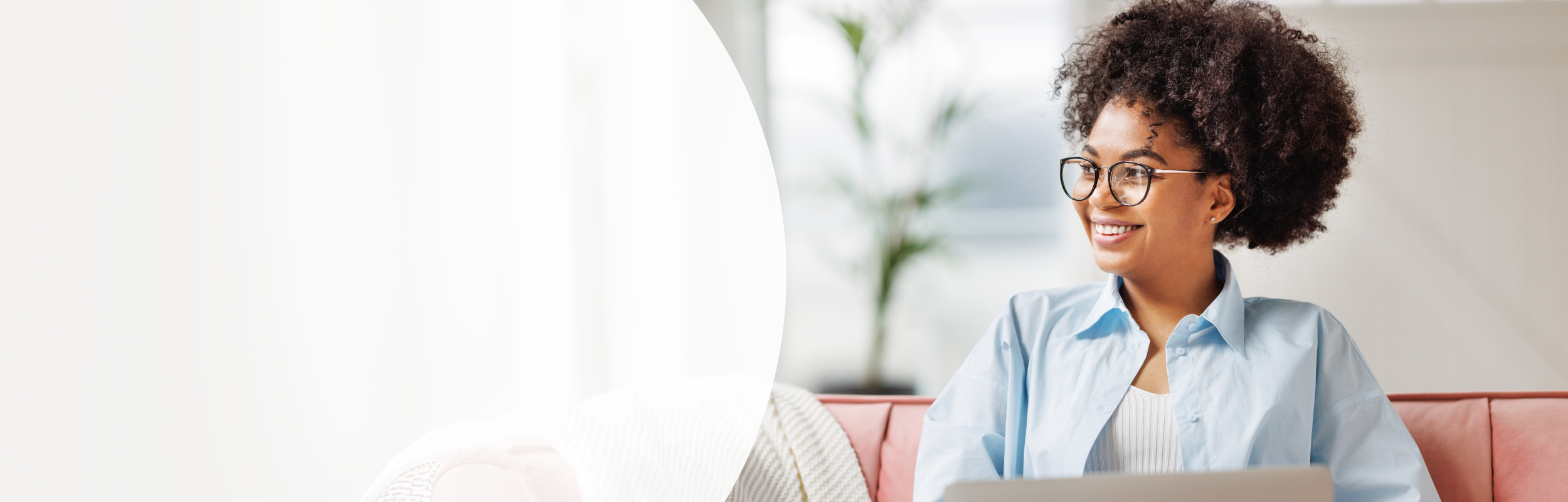 Junge lächelnde Frau mit Afro sitzt mit einem Laptop auf einer roten Couch