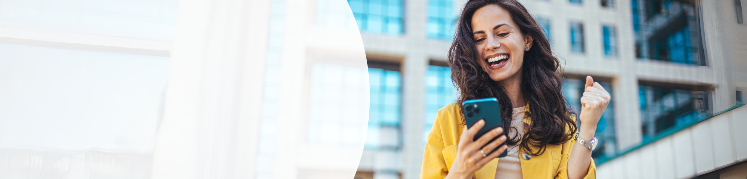 Frau mit langen brauen Haaren und gelber Jacke schaut voller Freude auf ihr Smartphone