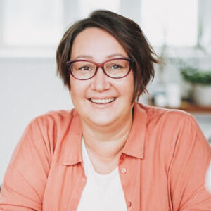 Portrait einer Frau mit kurzen braunen Haaren und einer orangenen Bluse.