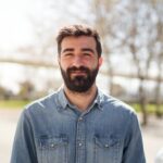 Portrait eines jungen bärtigen Mannes, der ein blaues Jeanshemd trägt.