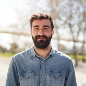 Portrait eines jungen bärtigen Mannes, der ein blaues Jeanshemd trägt.