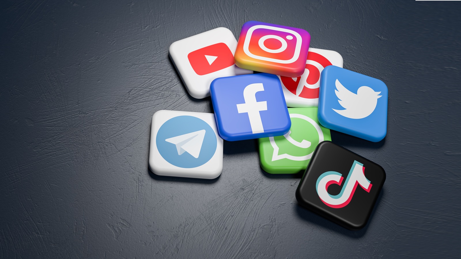 Logos einiger Social Media Plattformen (Youtube, Instagram & Co.) liegen auf einer dunkelgrauen Tischplatte