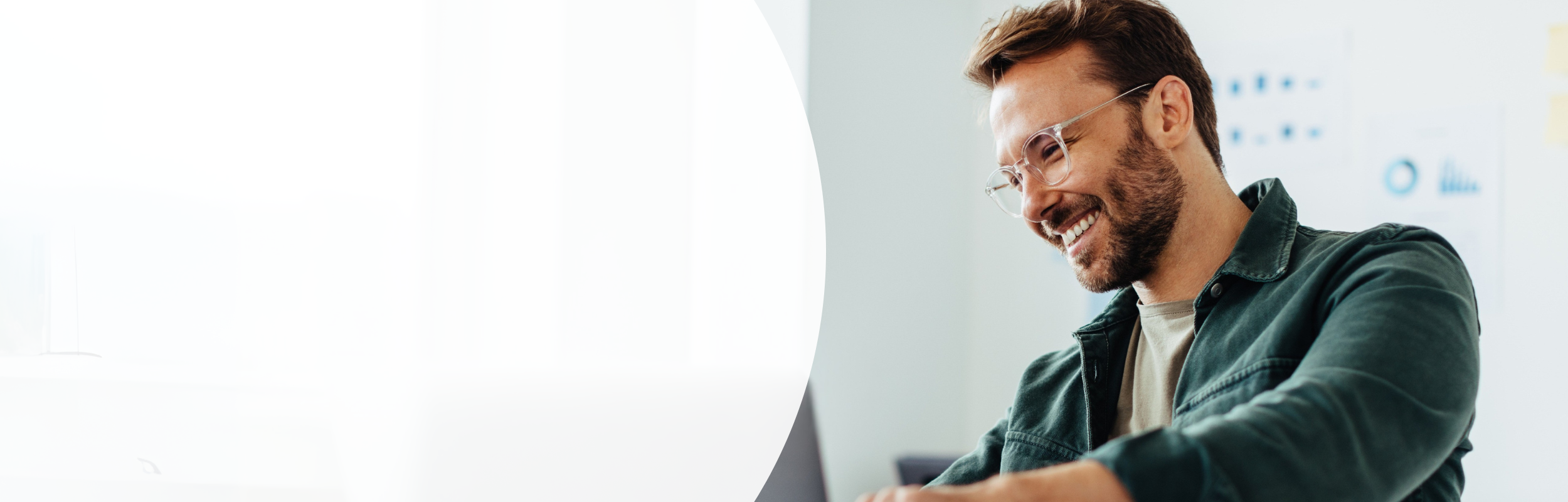 ein Mann mit Brille sitzt lächelnd vor einem silbernen Laptop.
