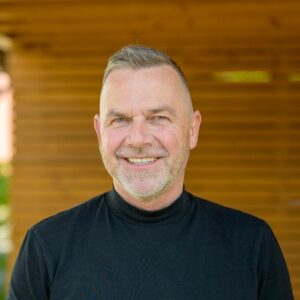 Mann mittleren Alters in einem schwarzen Pullover lächelt in die Kamera