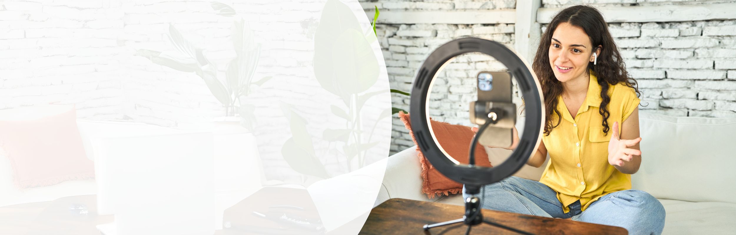 Eine junge Frau sitzt auf einem Sofa vor einem Ringlicht. Sie nimmt ein Video mit Smartphone auf.