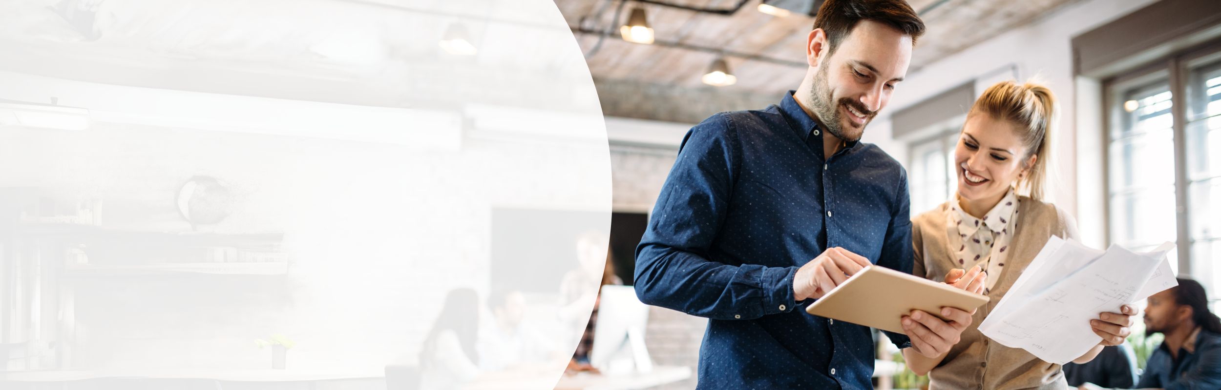 Eine Frau und ein Mann schauen in einem geschäftlichen Umfeld auf ein iPad, die Frau hält Zettel in der Hand.