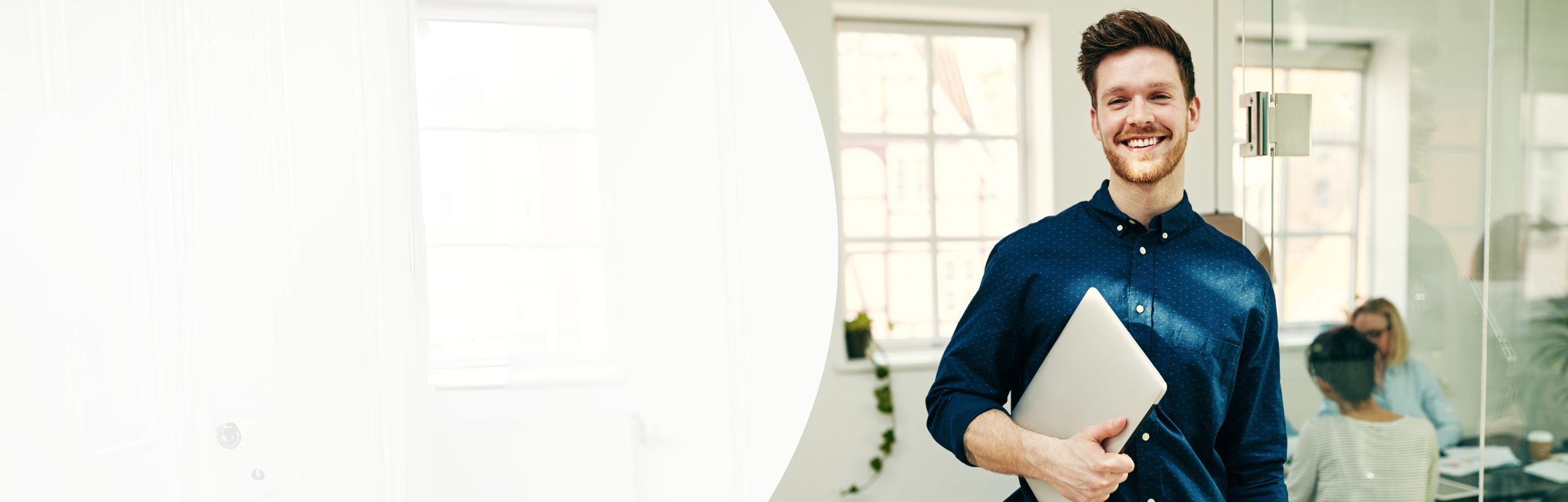 Mann in einem Büro mit blauem Hemd und Laptop in der Hand.