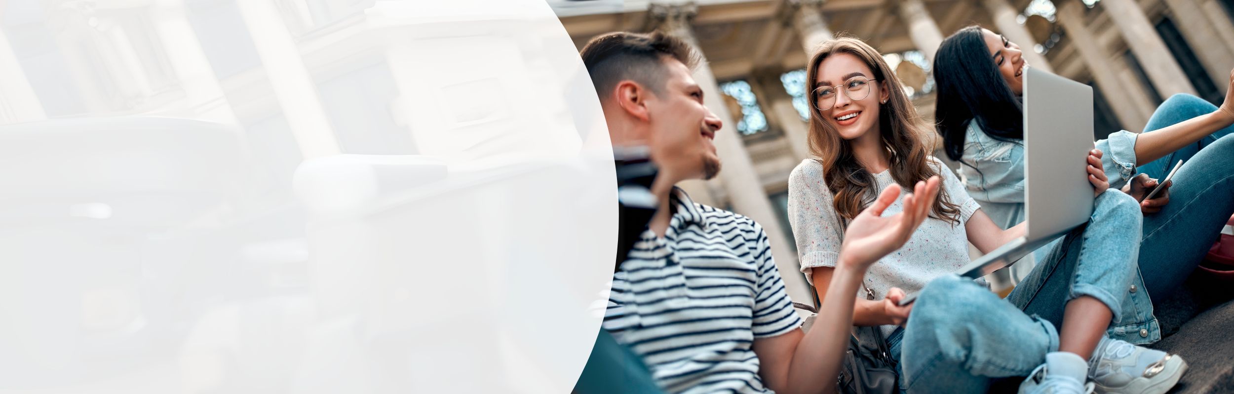 Drei junge Leute im Austausch im Freien – eine Person mit Laptop, zwei im Gespräch.