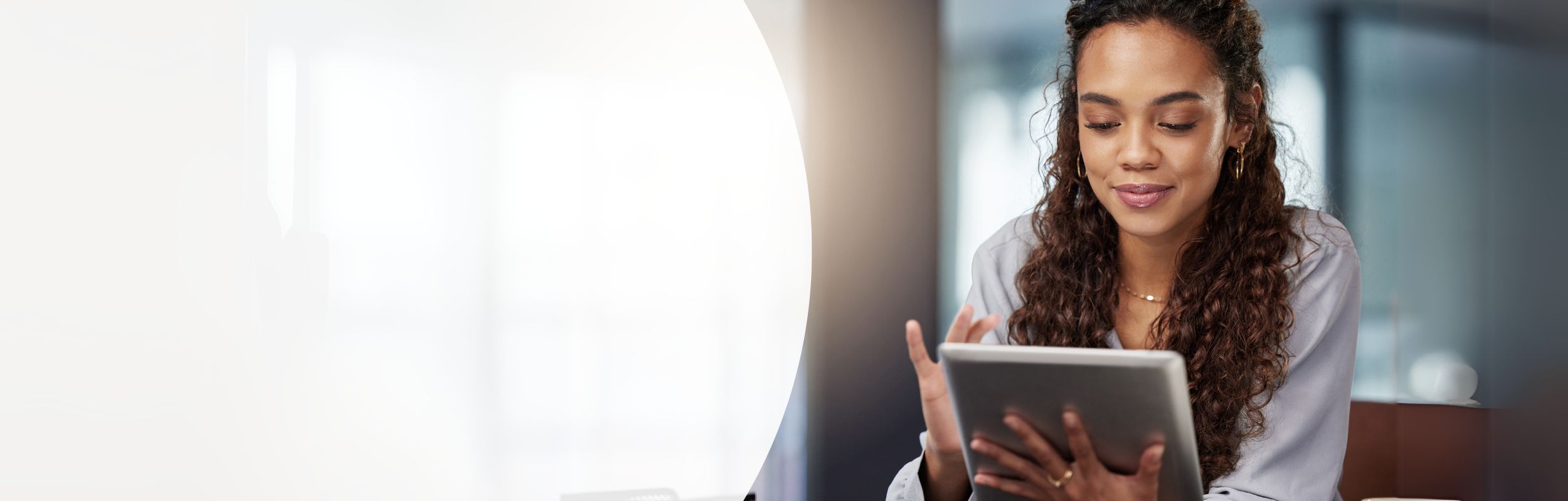 Frau mit langen brauen, lockigen Haaren blickt auf das Tablet in ihrer Hand.