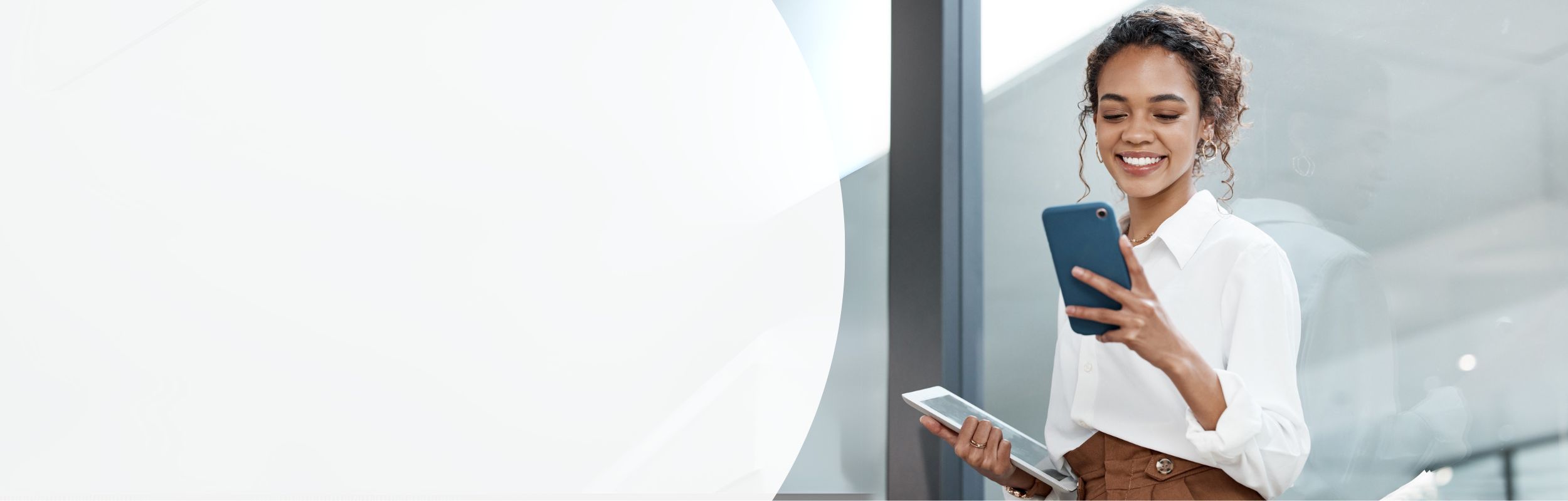 Frau im Geschäftsumfeld hält ein Tablet und ein Smartphone in den Händen.