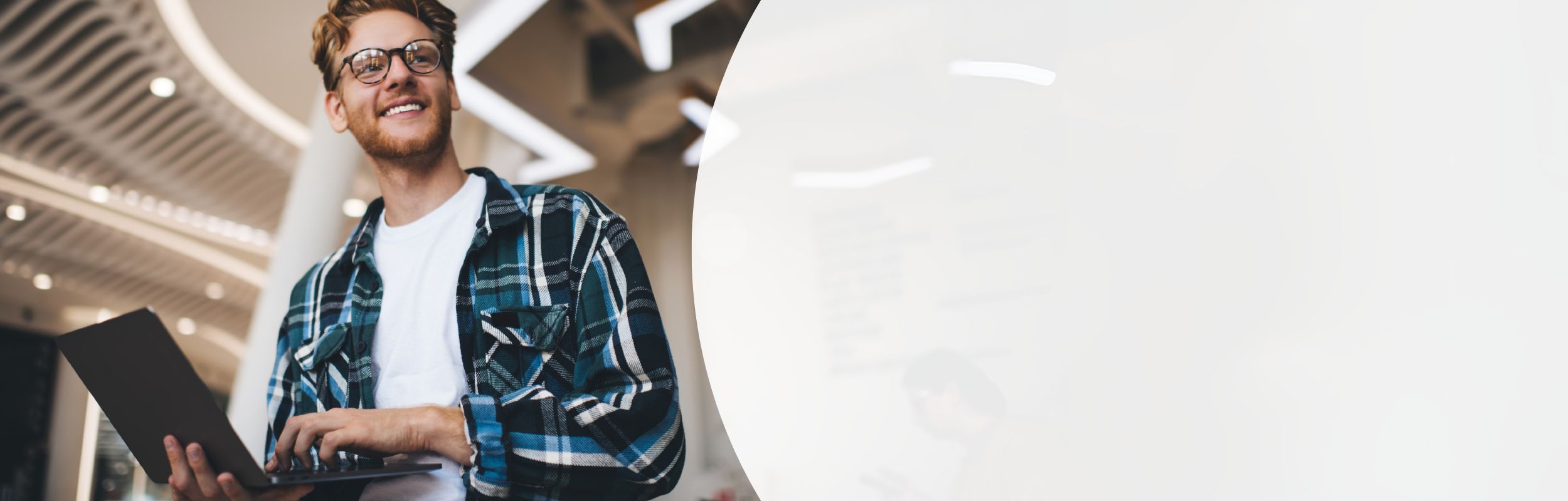 Mann mit Bart und Brille, trägt ein kariertes Hemd und hält einen Laptop in der Hand.