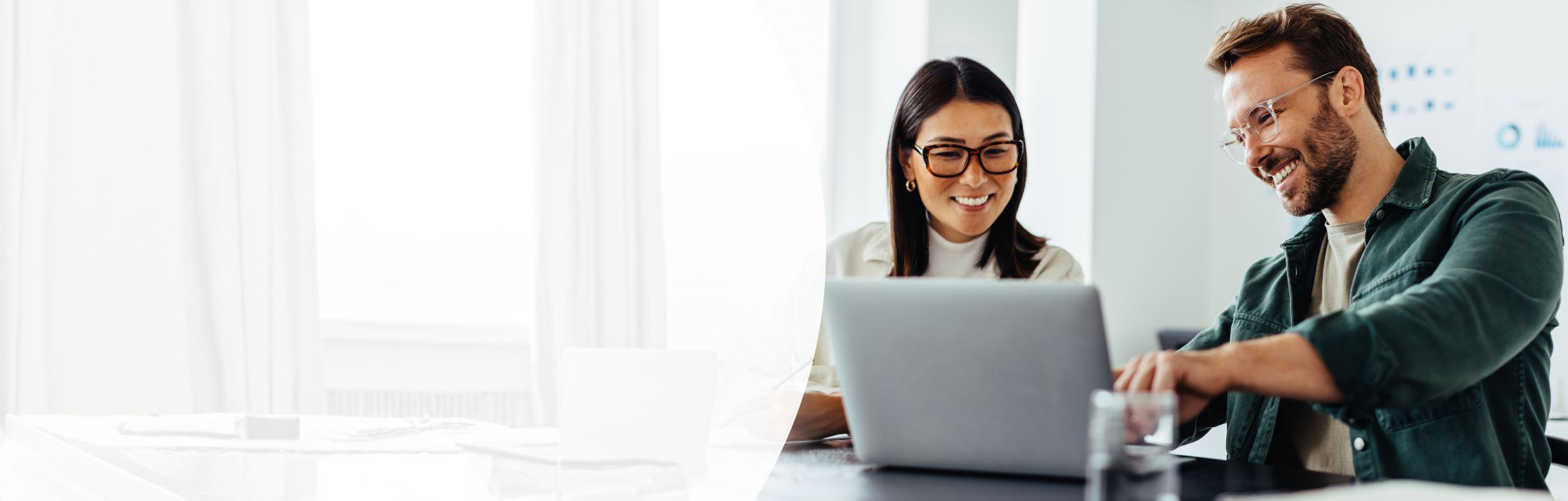 Ein Büromitarbeiter und seine Kollegin sitzen an einem Bildschirmarbeitsplatz.